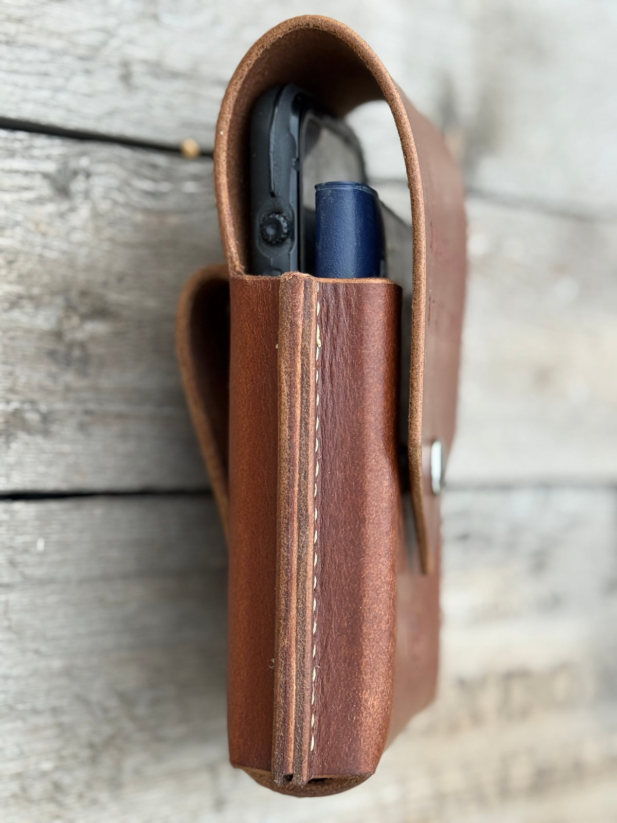 Brown leather case with a phone and notebook on a wooden surface