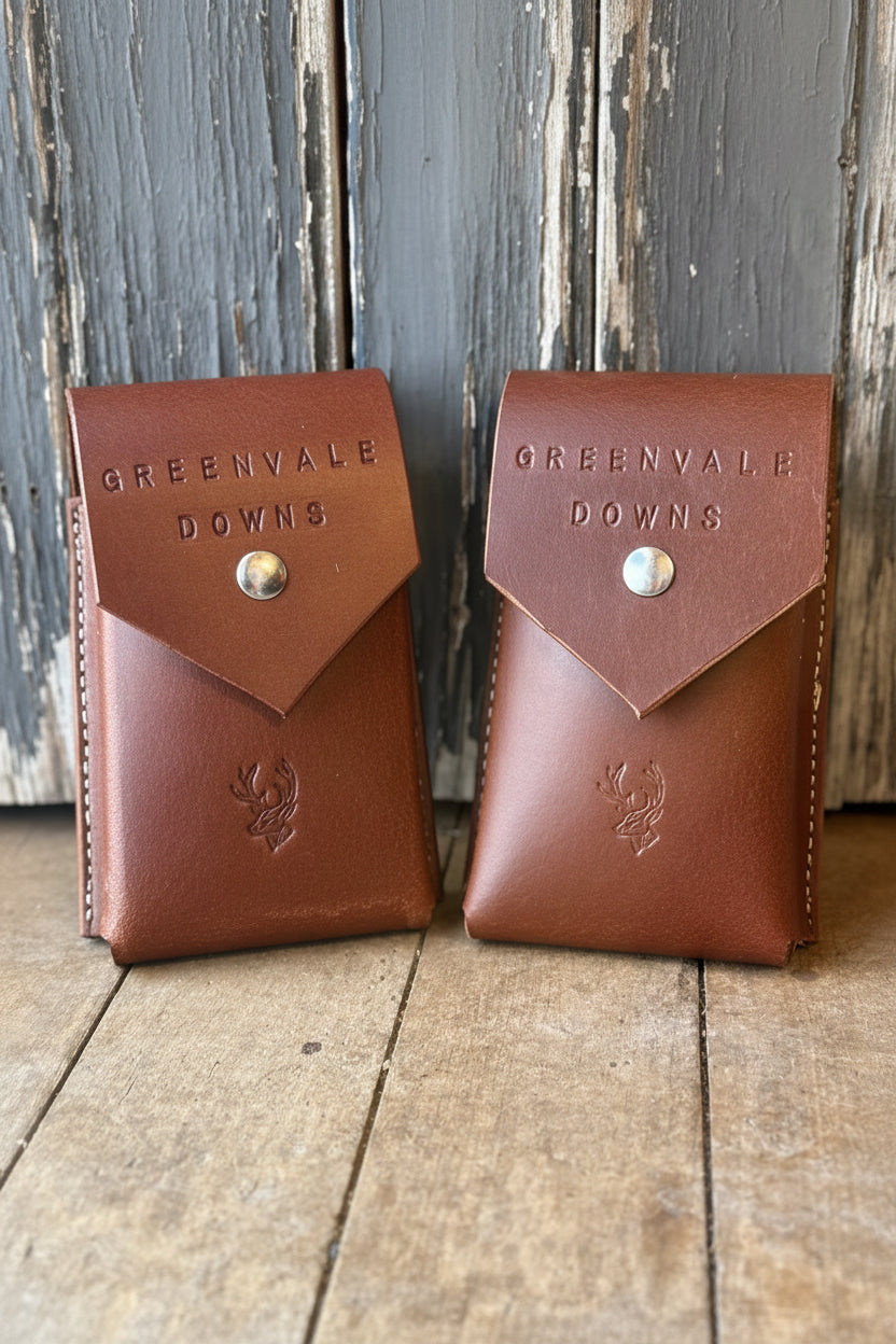 Two brown leather phone cases with 'Greenvale Downs' branding on a wooden surface.