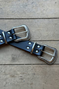 Black leather belt with silver buckles on a wooden surface
