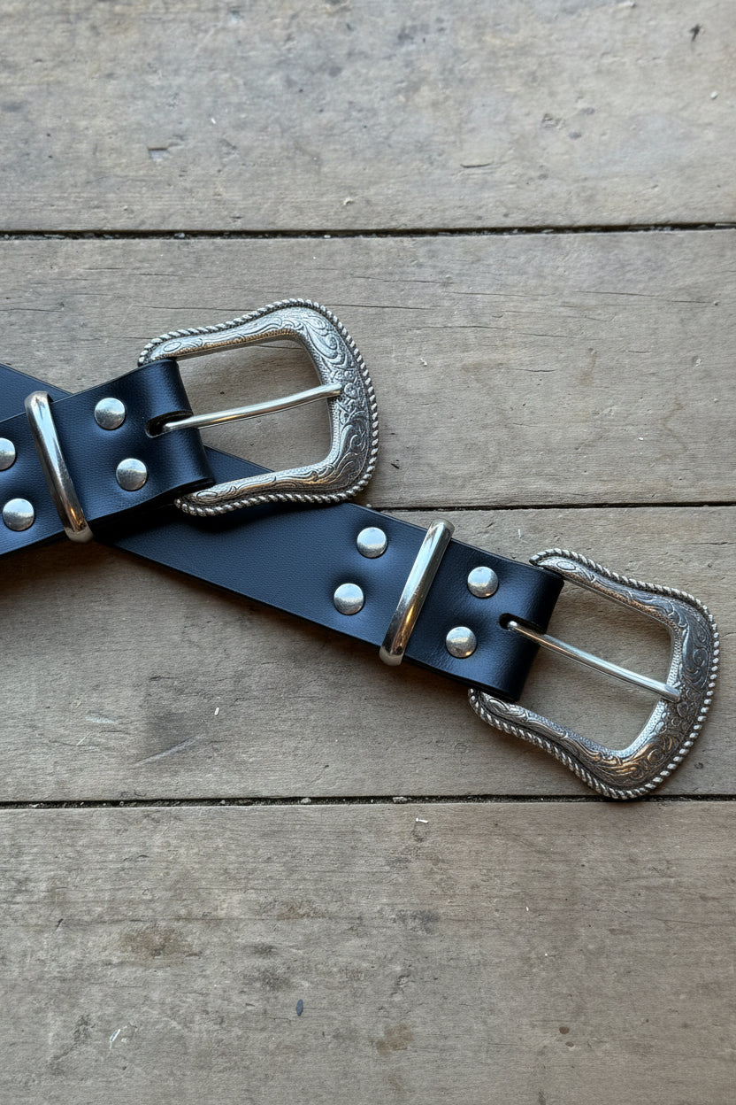 Black leather belt with silver buckles on a wooden surface